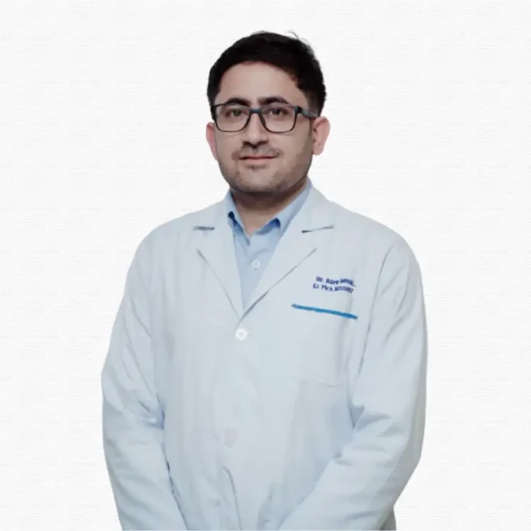 A man with glasses wearing a white medical coat stands against a plain background. He appears professional and approachable, with a slight smile.